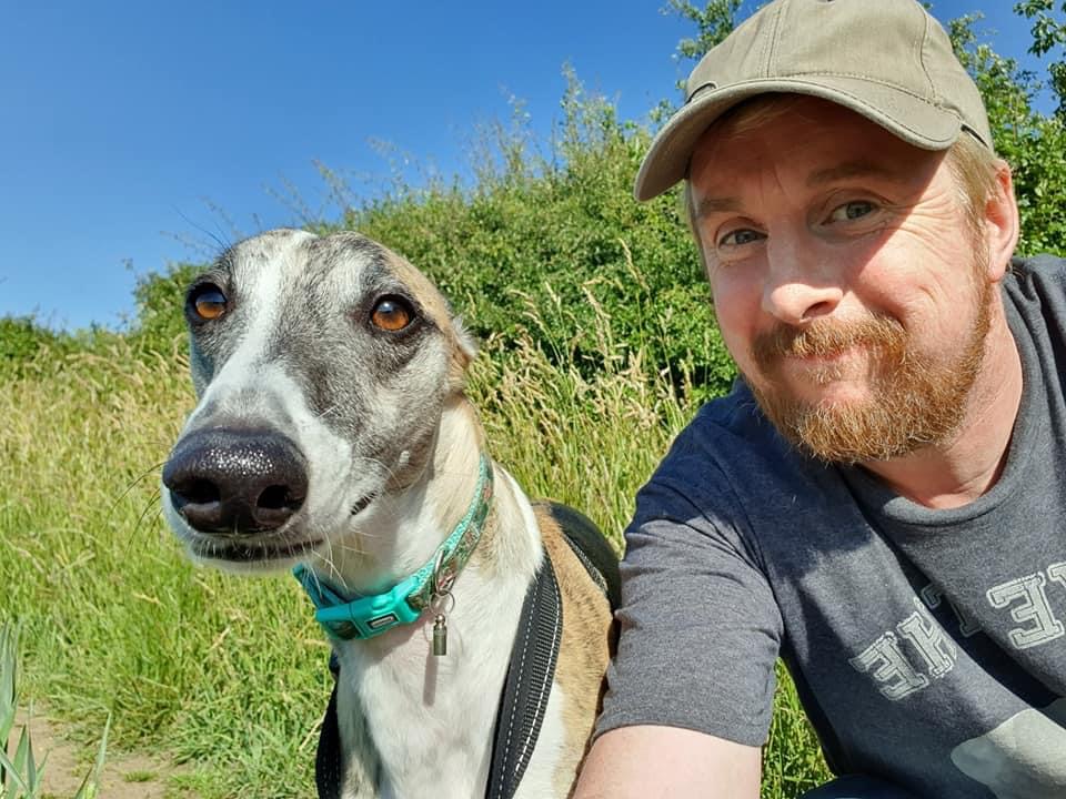 Photo show Paul James on the right wearing a khaki cap, to his right sits his dog, a brindle whippet named Twiglet